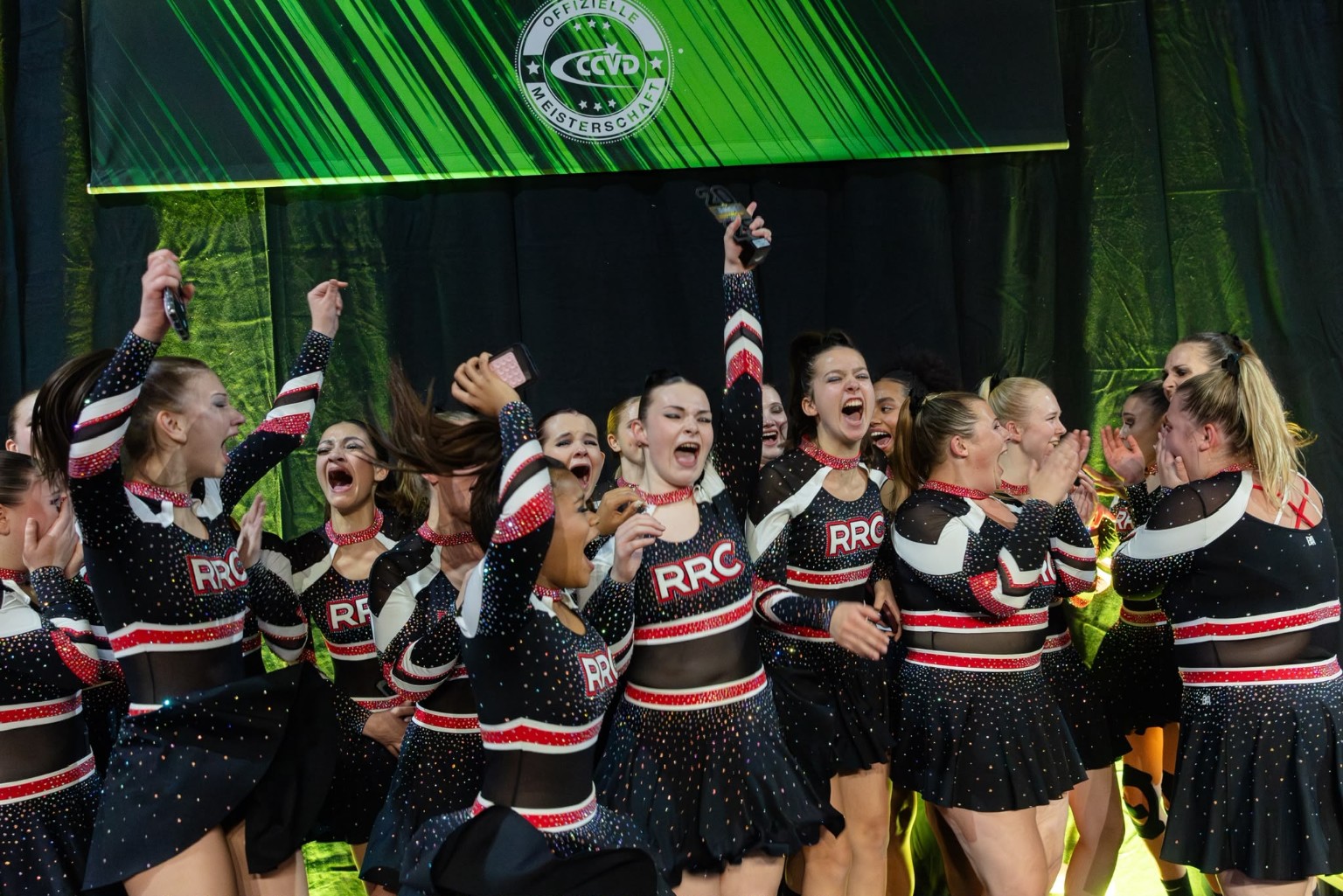 Die Rising Rockets jubeln gemeinsam mit einem Pokal bei einer Cheerleading-Meisterschaft.