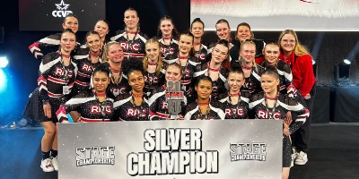 Die Rising Rockets im Wettkampfoutfit hinter einem Schild mit der Aufschrift Silver Champion.